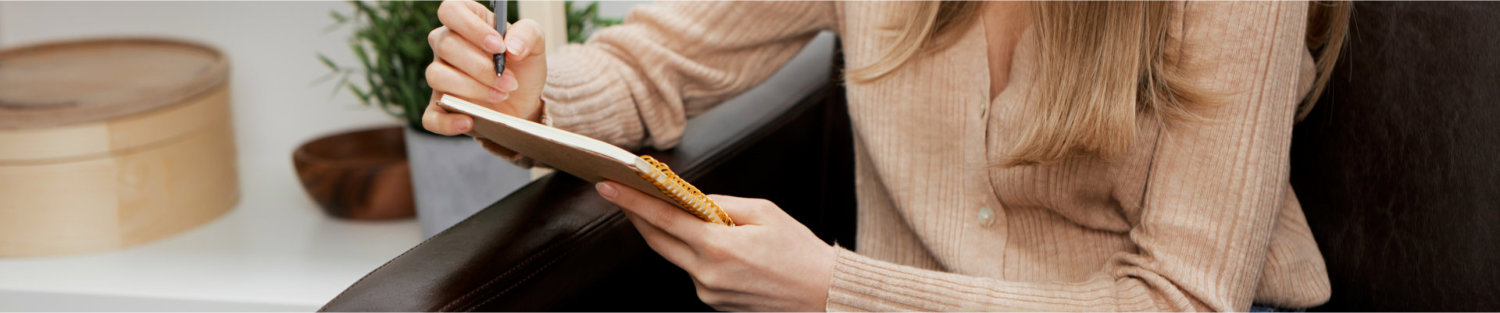 Focused cheerful blonde student lady with copybook write to do list sitting in sofa at modern living room interior. Female client have shrink appointment in a psychological help office. Copy space