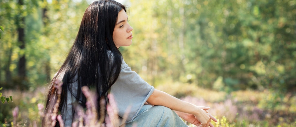 A young woman with long hair sits contemplatively among wildflow