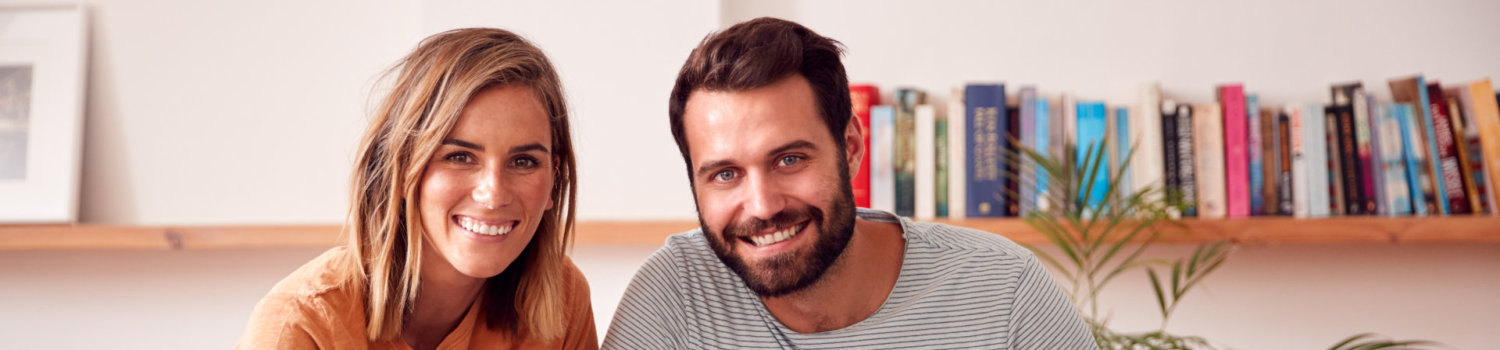 Portrait Of Loving Parents With Newborn Baby Lying On Bed At Home In Loft Apartment